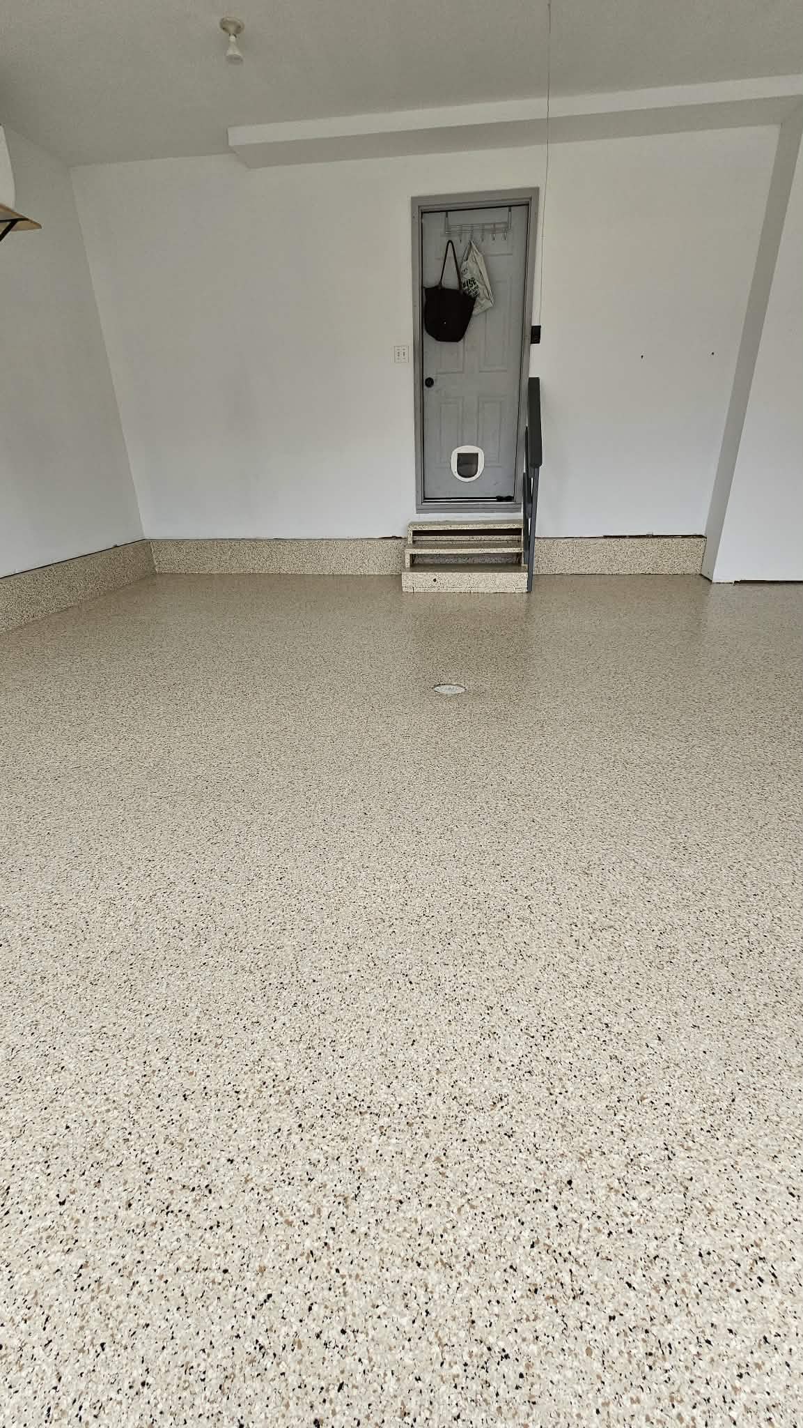 Tan, black and white flake epoxy garage floor in Liberty MO with coved wall base and coated service door step