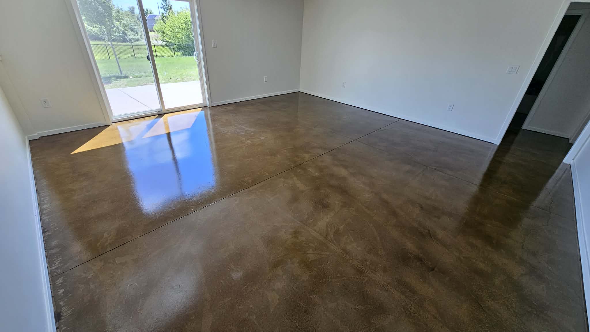Stained and sealed concrete floor in a 1,000 sq ft finished basement in Peculiar, MO, with sliding patio door