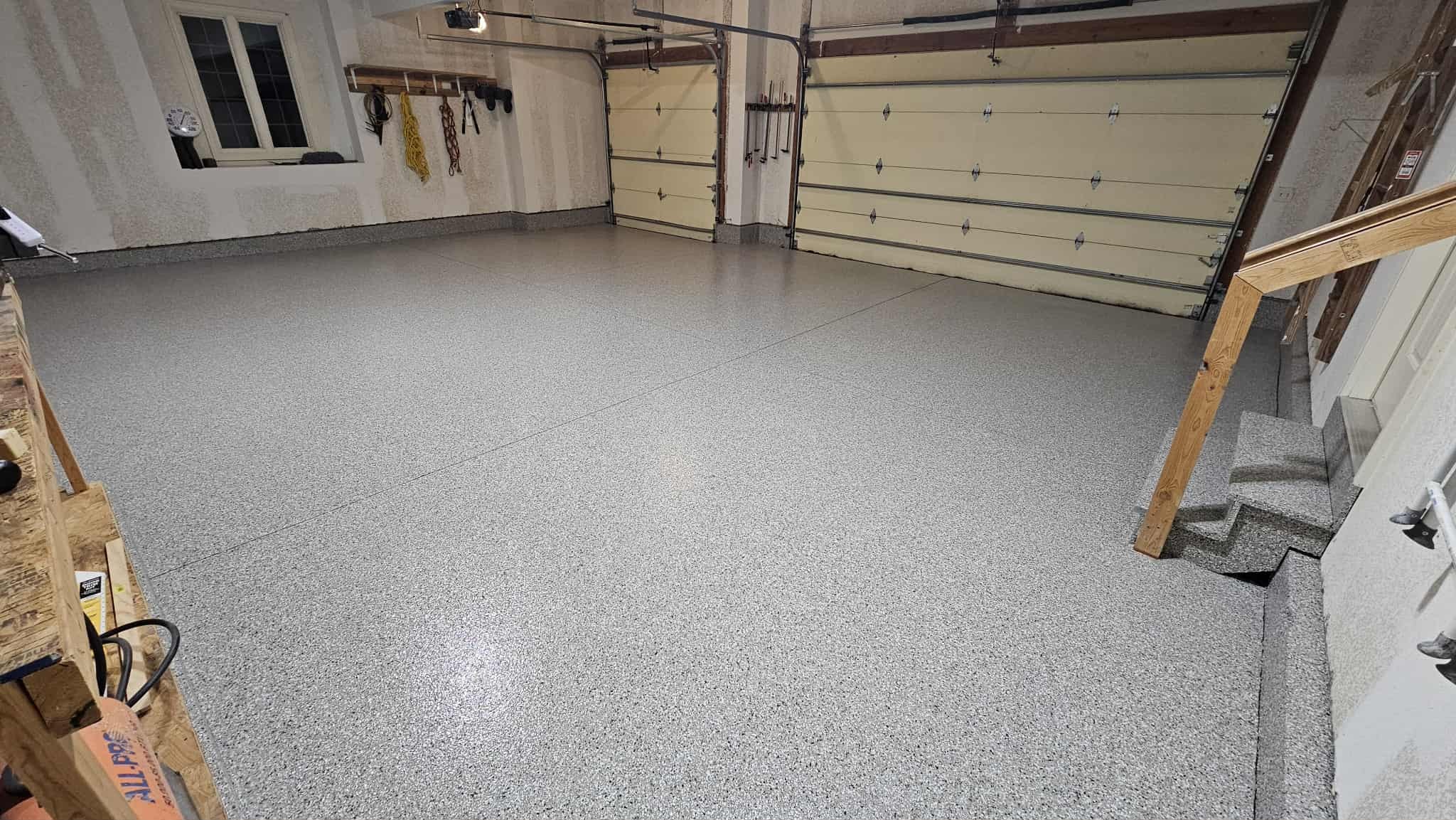 Gray flake epoxy garage floor in a Kansas City two-car garage with coated stairs and a workbench